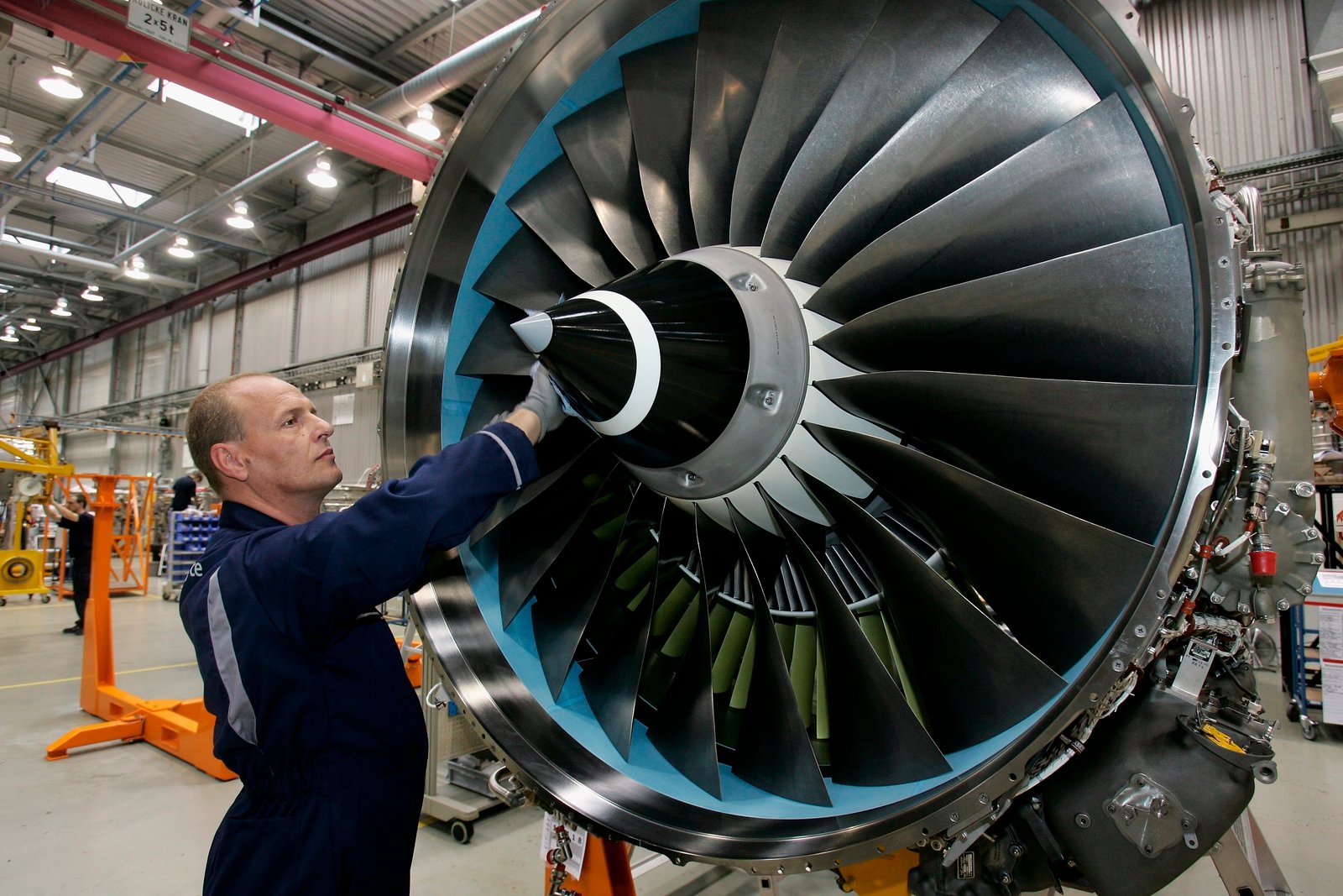 Ein Flugzeugmechaniker inspiziert die Schaufelblätter eines großen Triebwerks in einer Wartungshalle.